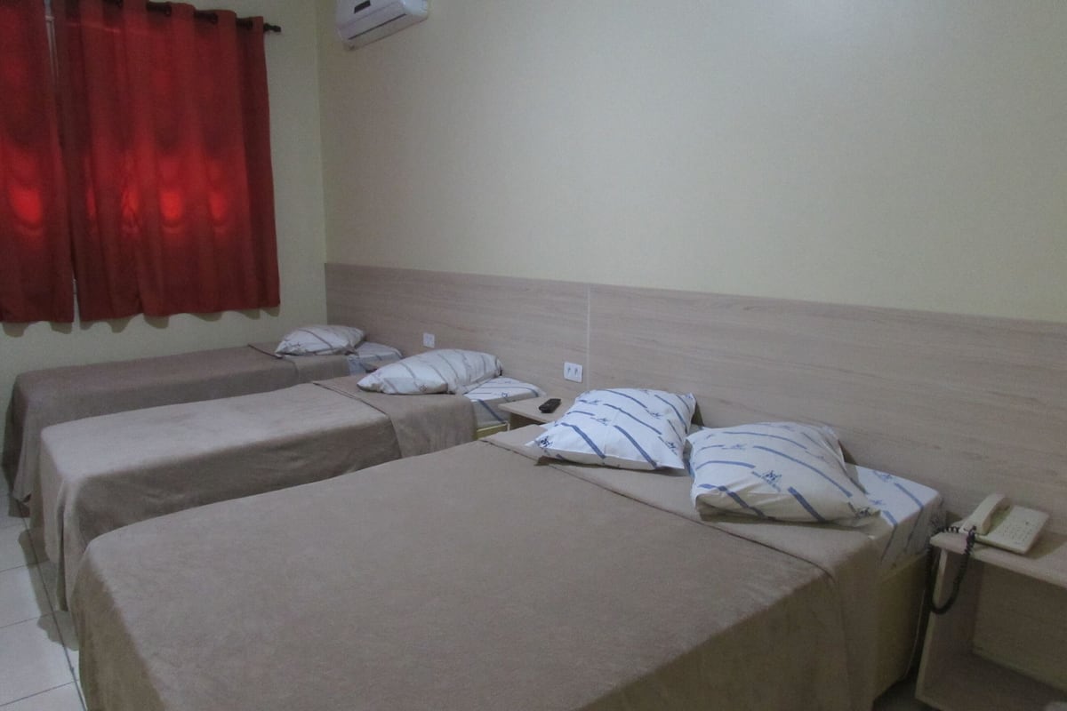 Une chambre d’hôtel avec deux lits simples, chacun équipé d’un oreiller et d’une couverture. On y trouve une table de chevet avec un téléphone et un climatiseur fixé au mur.