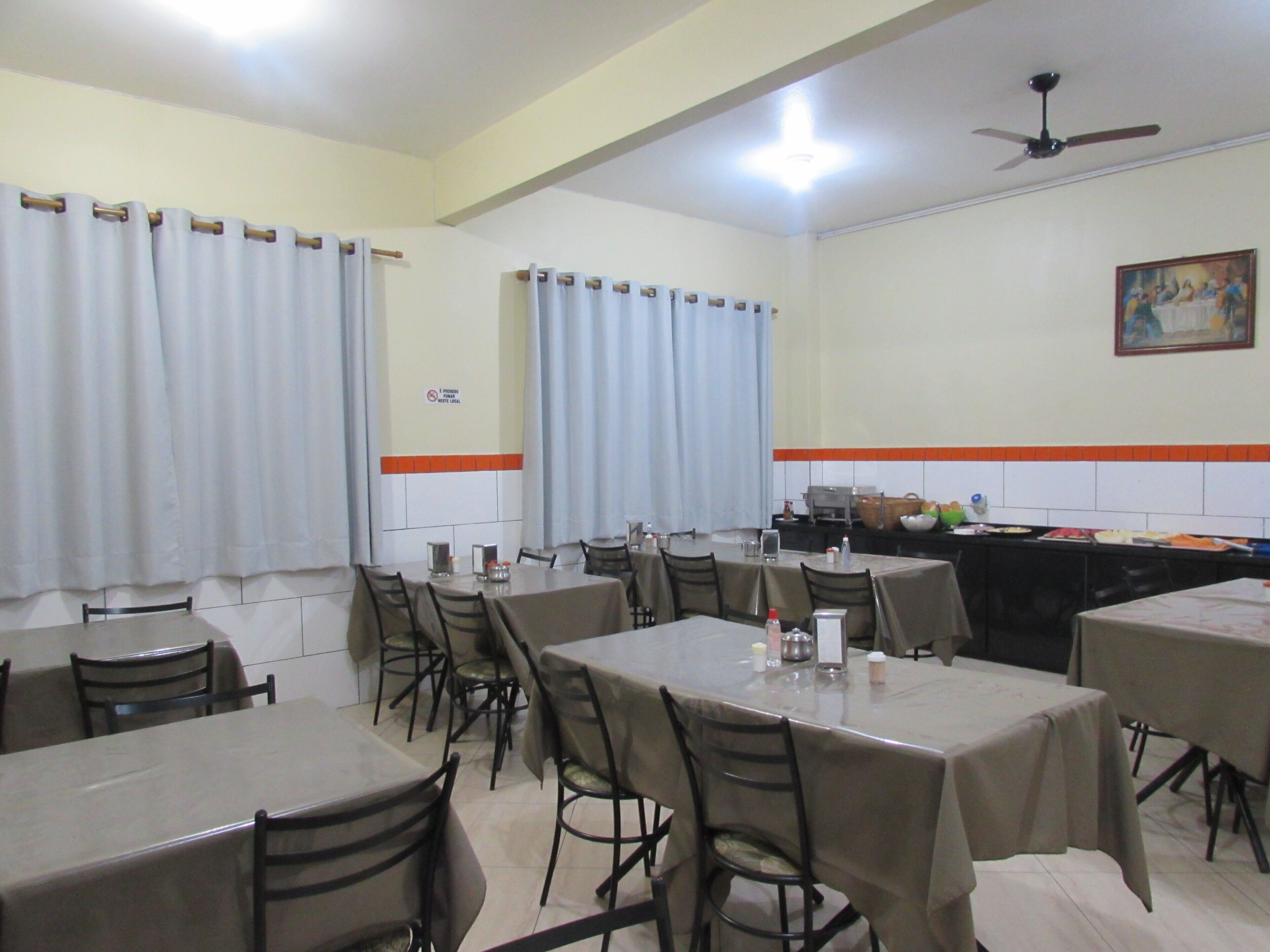 A dining area with multiple tables and chairs, a ceiling fan, and a kitchen counter visible in the background.