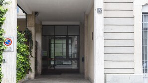 Une entrée d’immeuble avec un panneau indiquant qu’il est interdit de se garer, un pilier en béton et une porte en verre.