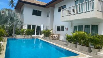 Una casa moderna de dos pisos con piscina, rodeada de plantas en macetas y palmeras.