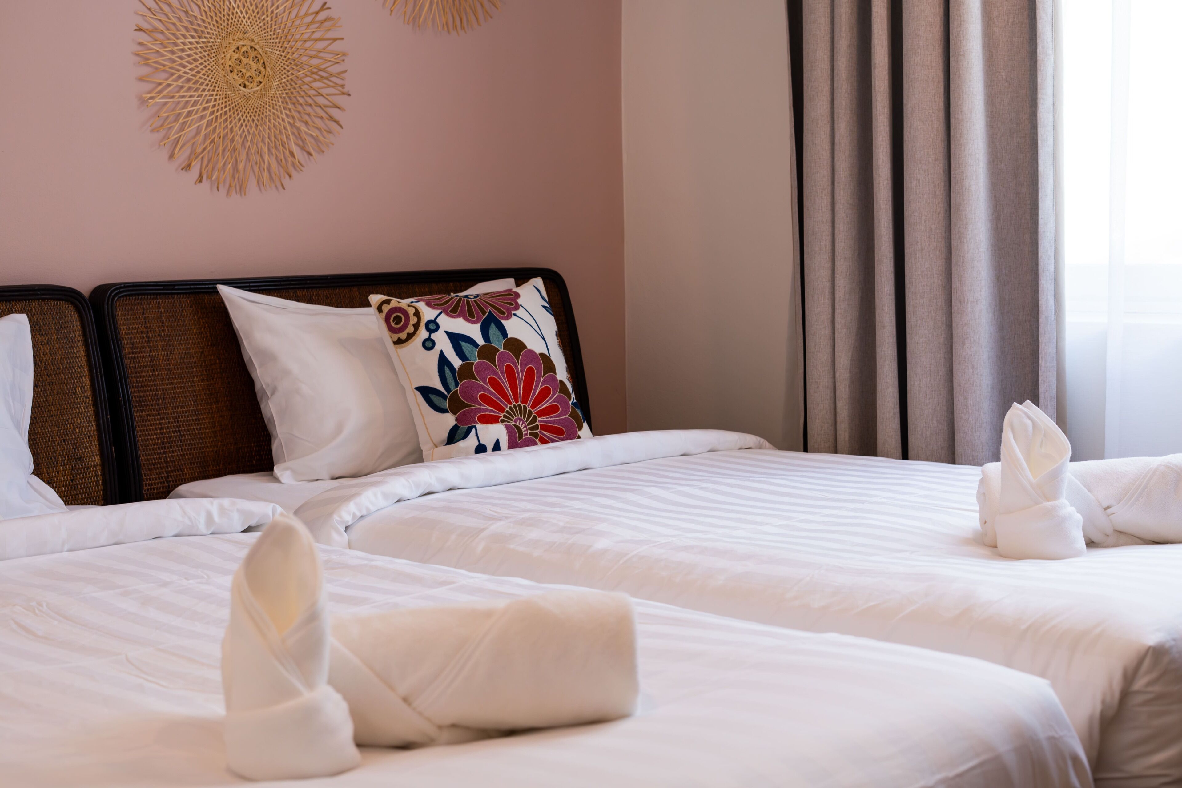 A hotel room with two beds, white linens, a floral pillow, and a decorative wall hanging.