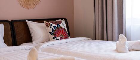 A hotel room with two beds, white linens, a floral pillow, and a decorative wall hanging.