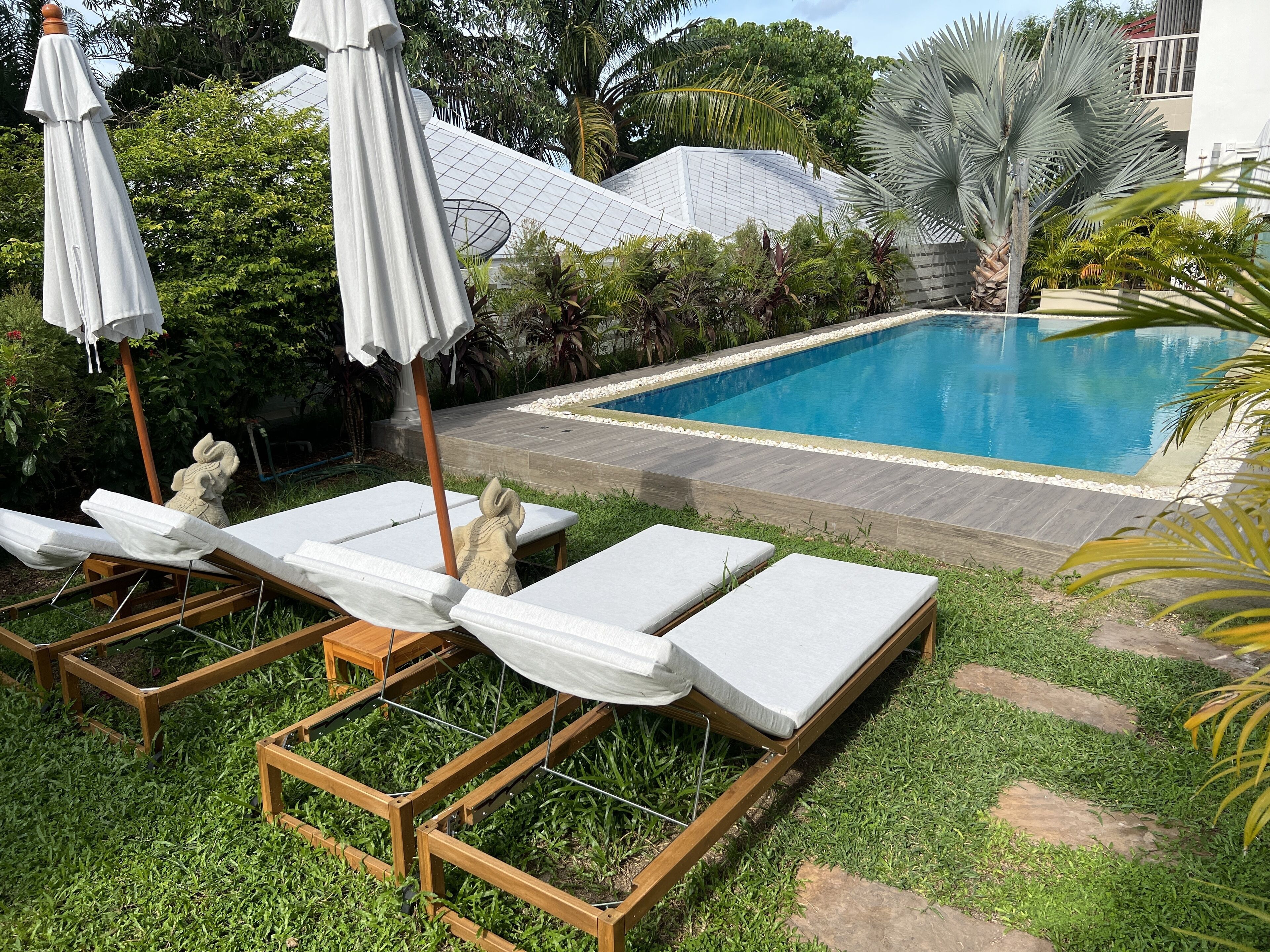 Ein Swimmingpool mit Liegestühlen und Sonnenschirmen, umgeben von Grünflächen und einem Gebäude mit Glasdach.