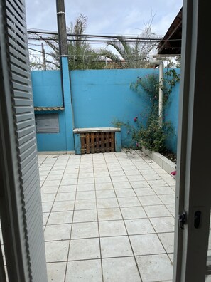 A tiled patio with a blue wall, a wooden bench, and a white pipe. - Kandui Flats Maresias (São Sebastião)