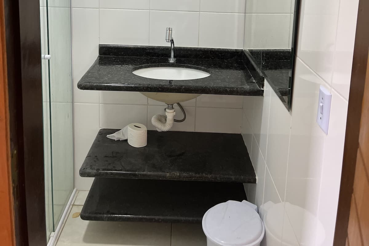Ein kleines Badezimmer mit weißen Fliesen, einem schwarzen Waschtisch, einem Spiegel und einer Toilette.