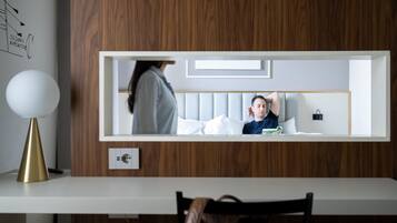 Camera d'albergo moderna con una parete in legno, un comodino bianco, una lampada e un letto con una persona che legge un libro.