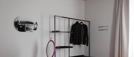 A modern bedroom with a bed, a vanity with a mirror, a pink chair, a black coat rack, and a decorative ceiling.
