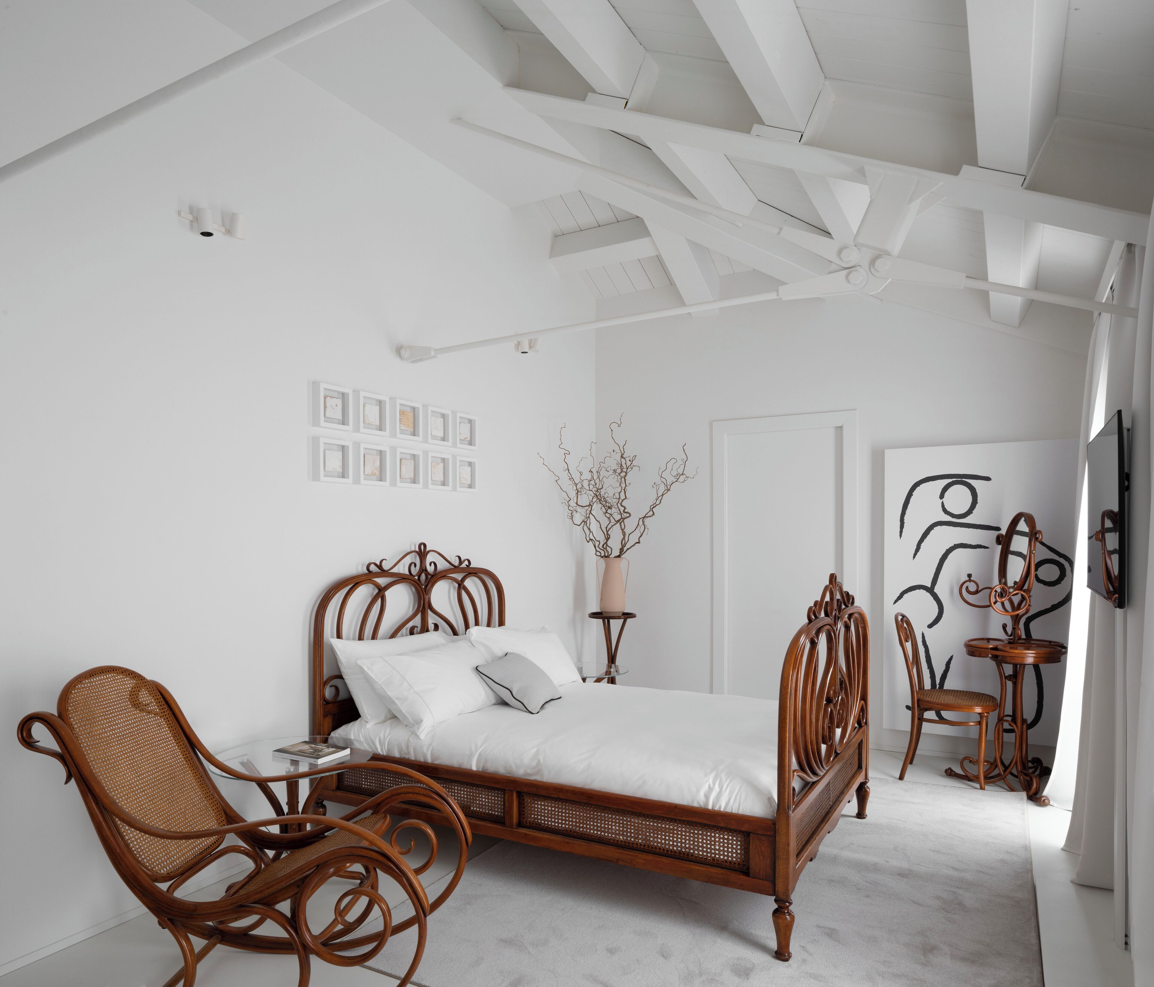 Ein Schlafzimmer mit einem hölzernen Bett, einem Korbstuhl, einem kleinen Tisch und einer dekorativen Vase.