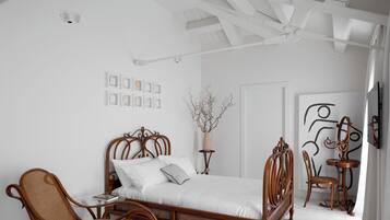 Ein Schlafzimmer mit einem hölzernen Bett, einem Korbstuhl, einem kleinen Tisch und einer dekorativen Vase.