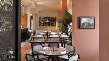 A modern dining area with round tables and chairs, a long counter, and a large plant.