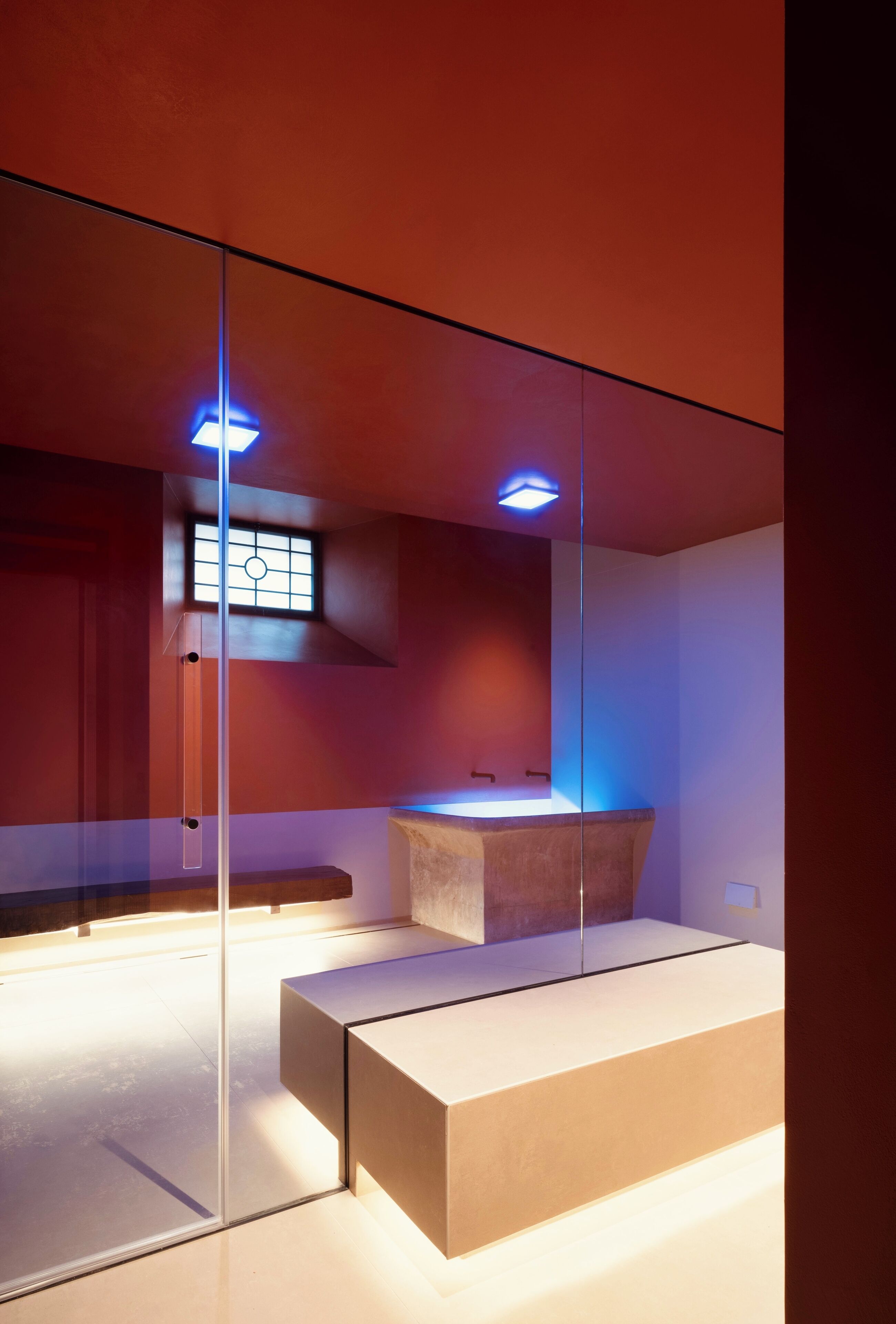 A modern bathroom with a glass partition, a wooden bench, and a built-in sink.