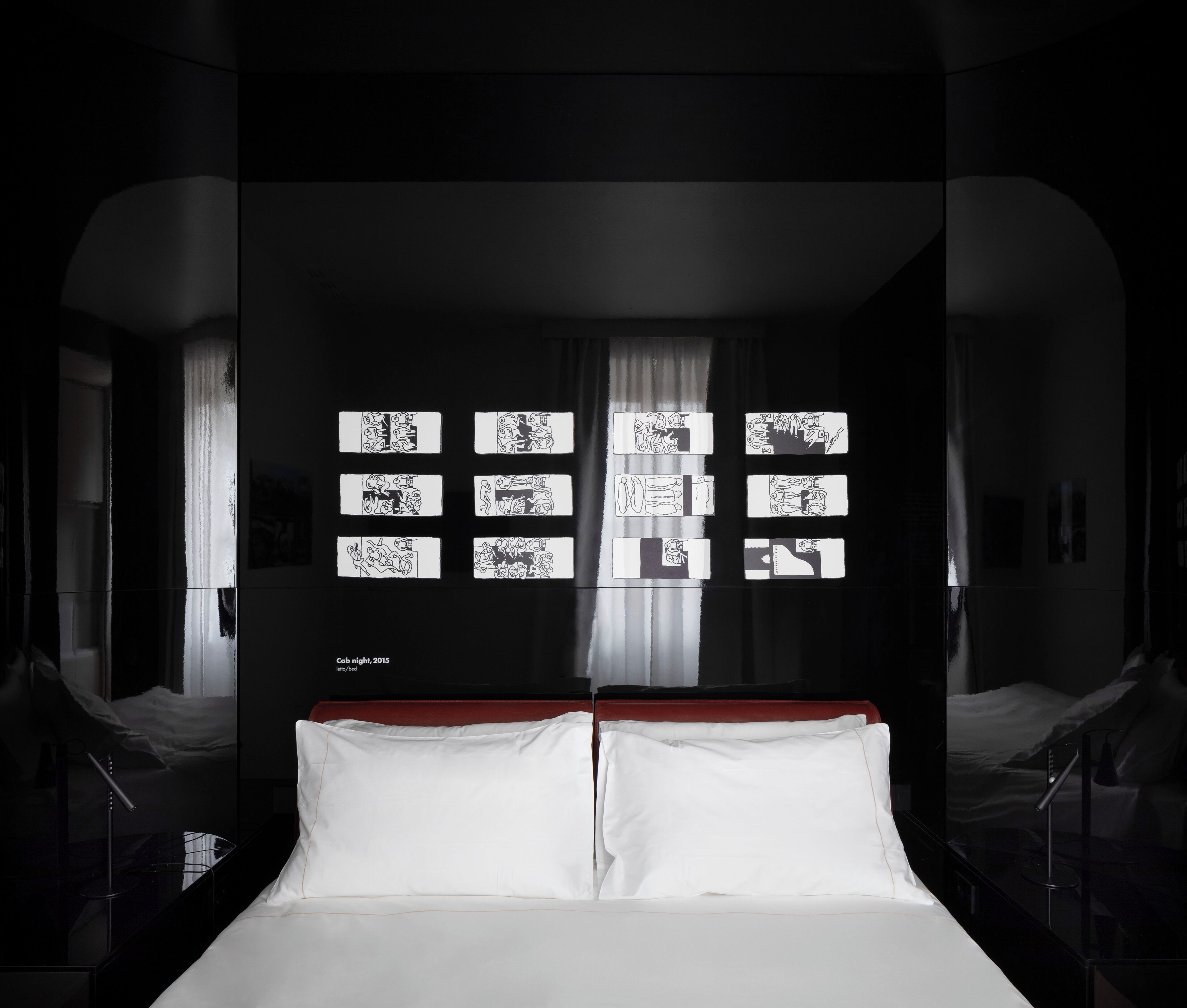 Een moderne hotelkamer met een groot bed, een rood hoofdeinde en een muur met meerdere zwart-wit kunstwerken.