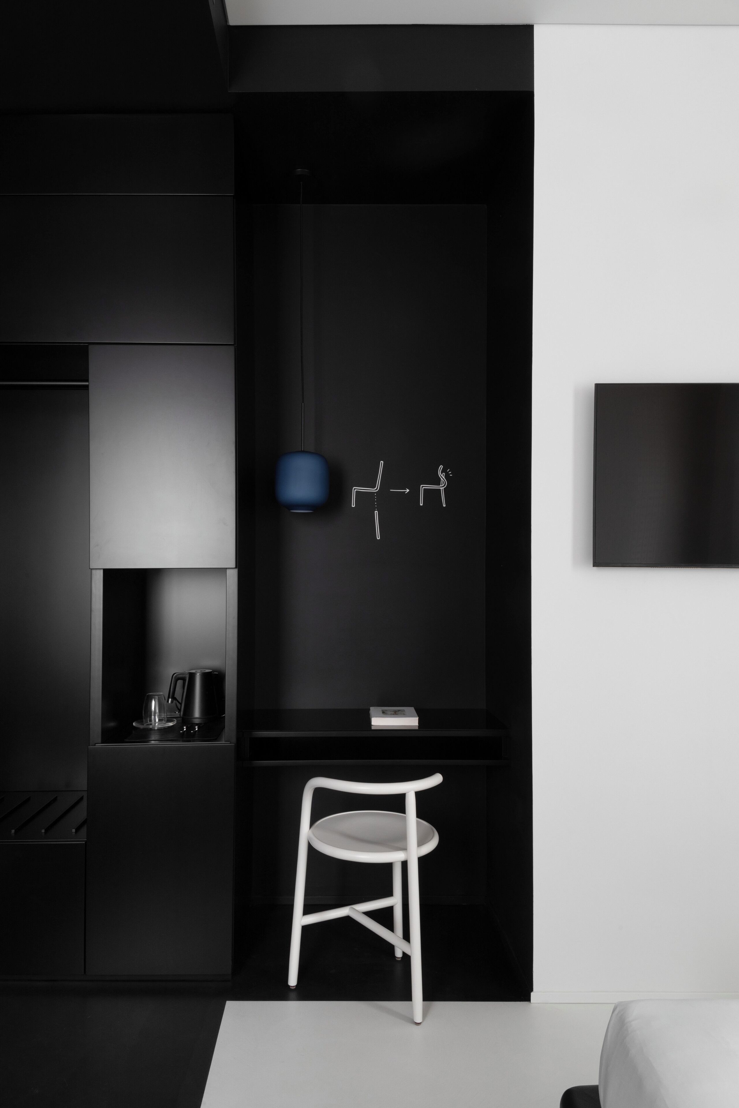 Een moderne, minimalistische kamer, uitgevoerd in zwart-wit, met een bureau, stoel en een wandlamp.