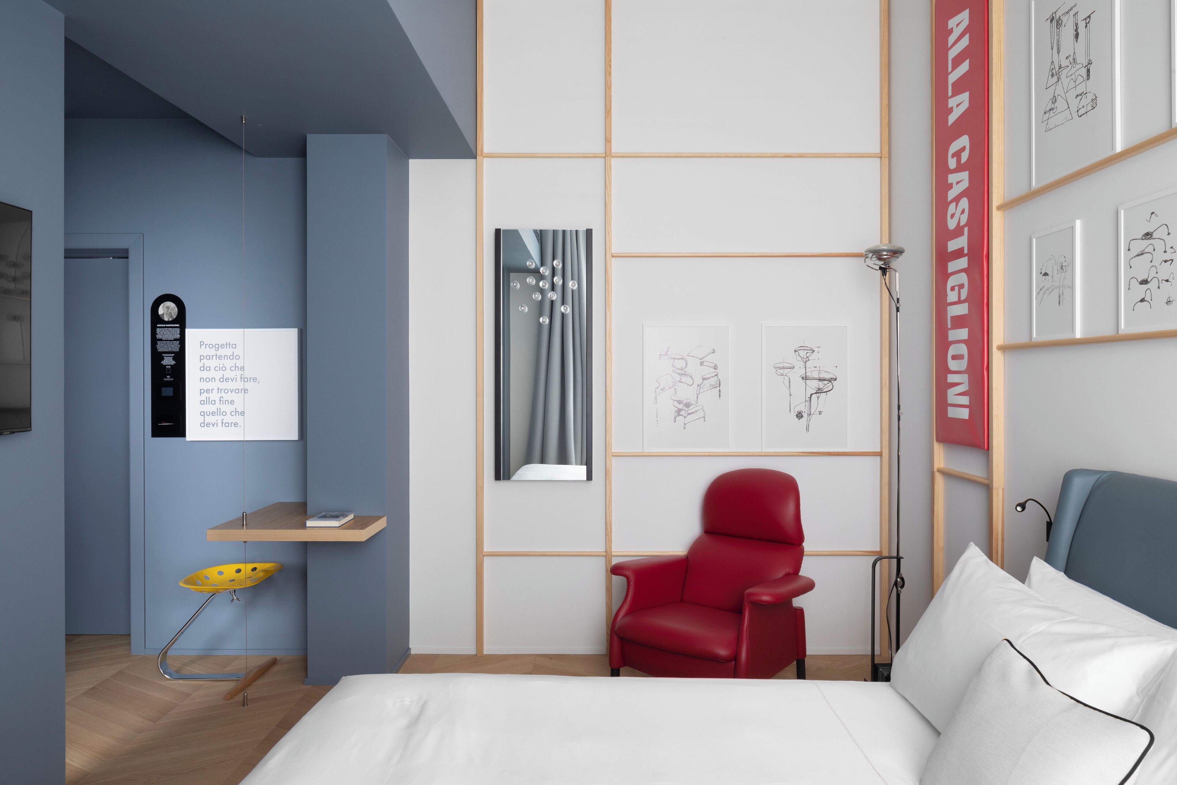Una habitación de hotel moderna con una cama, una silla roja, un escritorio con silla y obras de arte en las paredes.