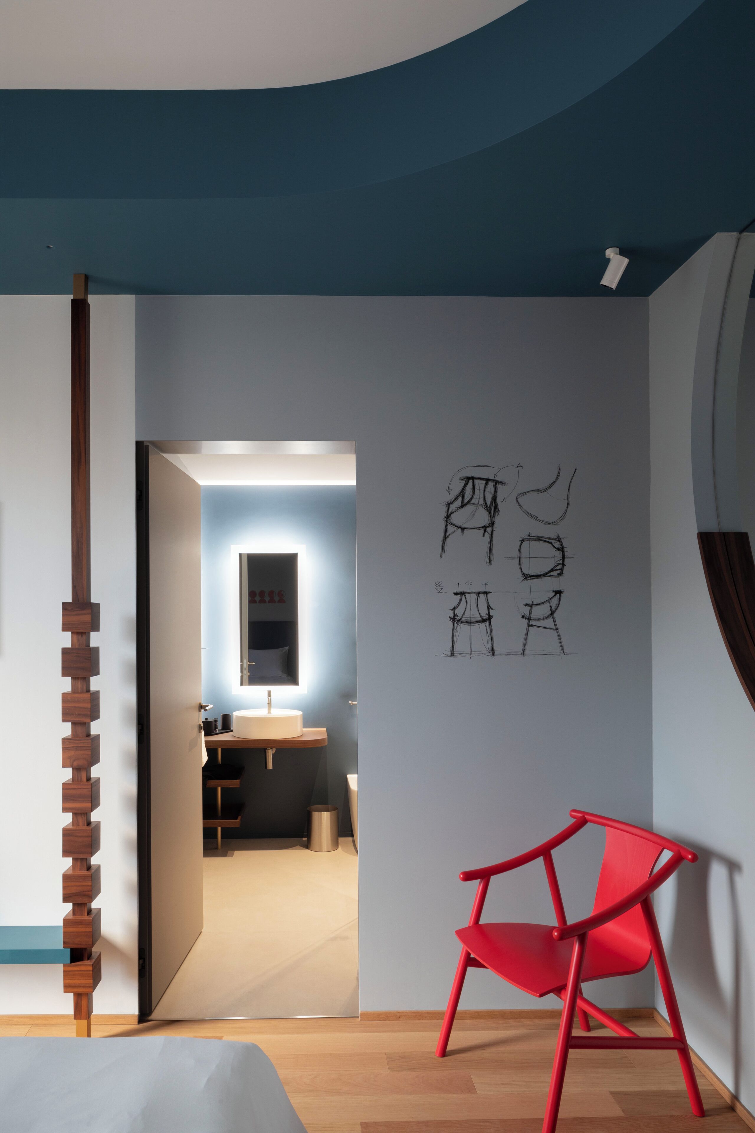 A modern interior with a wooden floor, a red chair, and a wall with sketches.