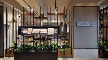 A reception area with a modern design, featuring a black reception desk, vertical black metal panels, and a sign reading "L'OPIFICIO".