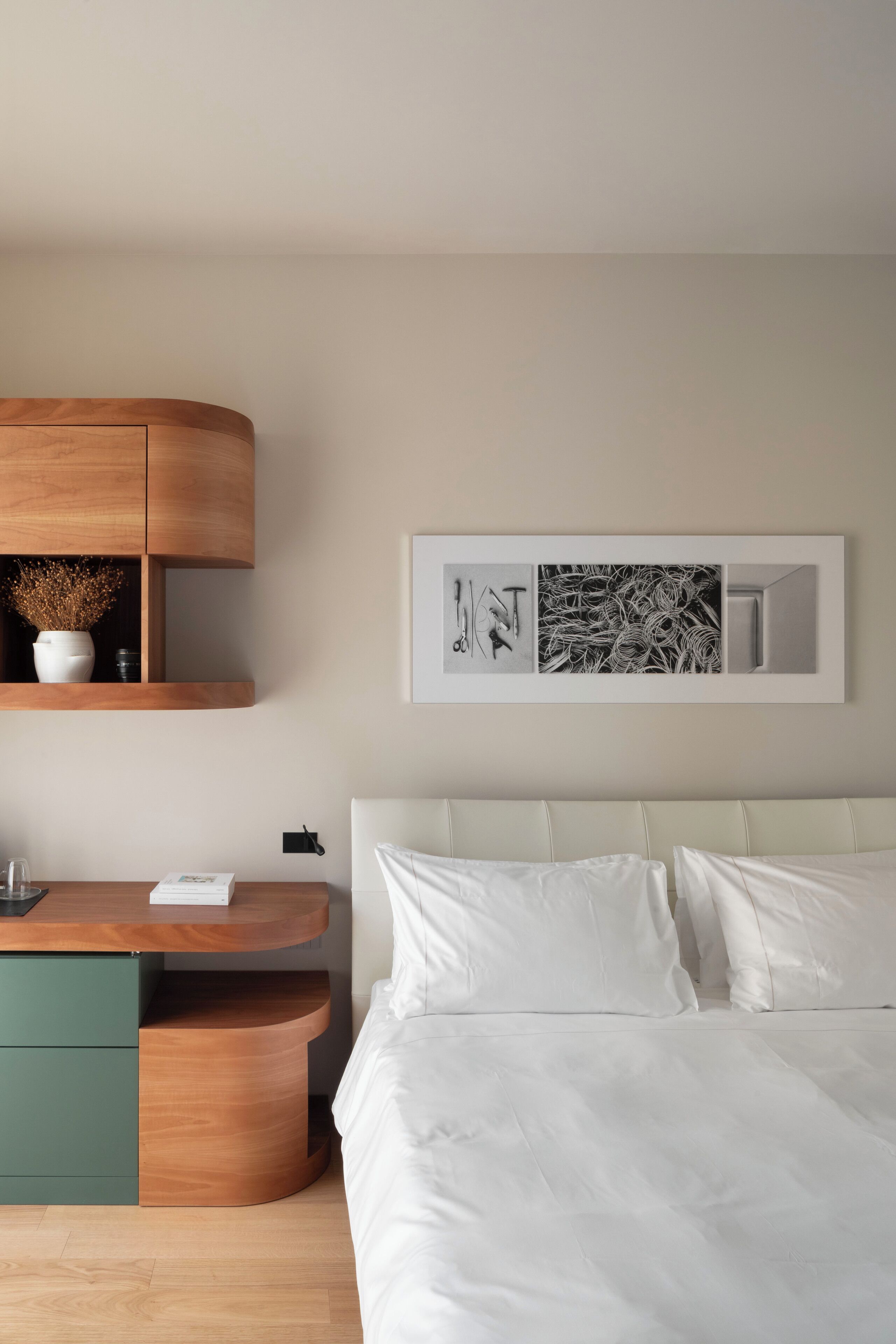 A bedroom with a bed, a wooden nightstand, a green drawer unit, and a wall-mounted shelf with decorative items.