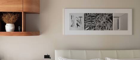A bedroom with a bed, a wooden nightstand, a green drawer unit, and a wall-mounted shelf with decorative items.