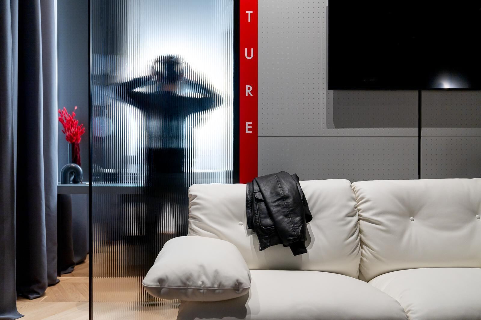 A modern living room with a white sofa, a black jacket draped over it, and a large window with vertical blinds.