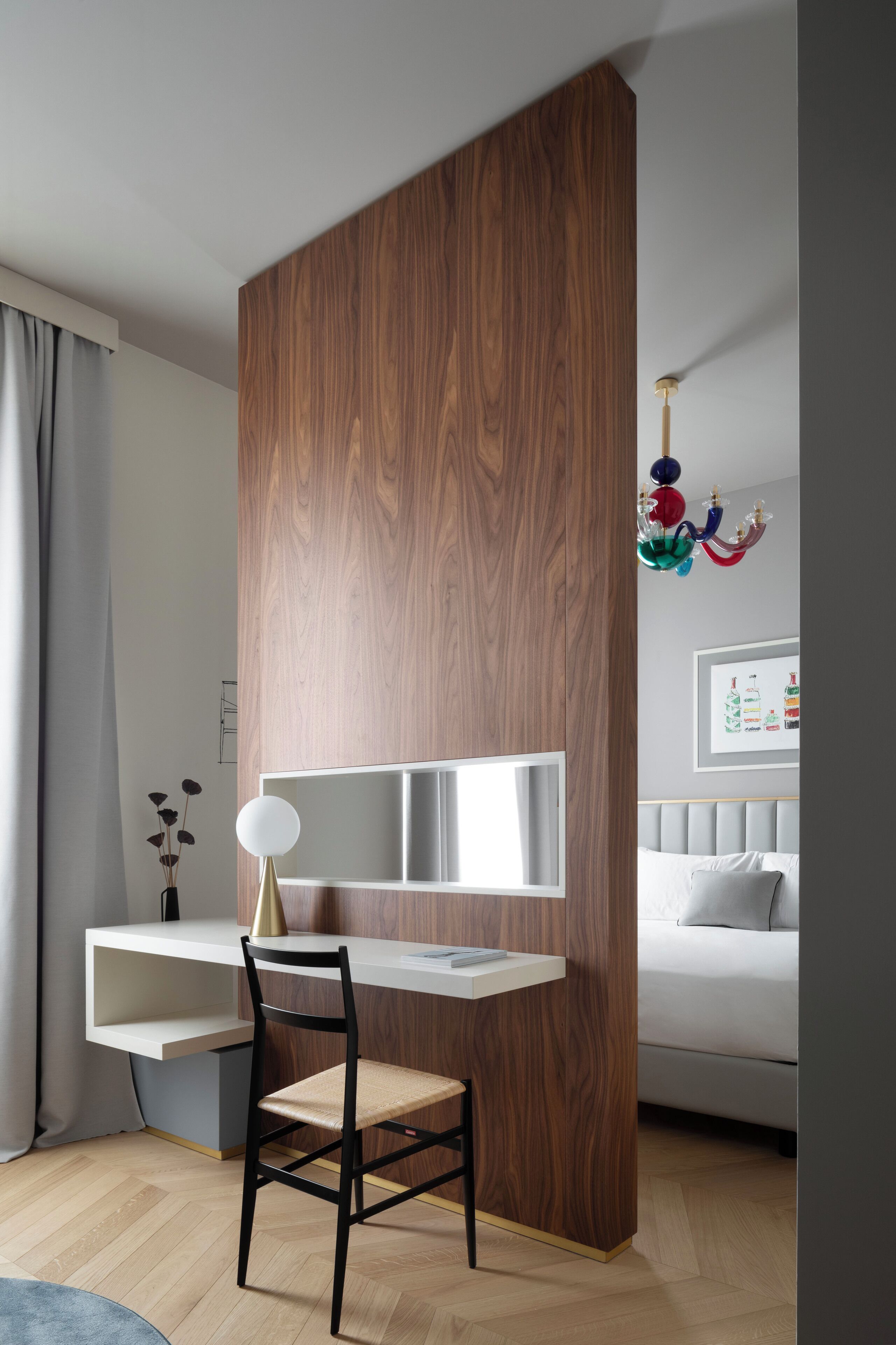 Ein modernes Schlafzimmer mit einer Holzwand, einem Schreibtisch mit Stuhl, einem Bett mit grauem Kopfteil und einer Chandelier.