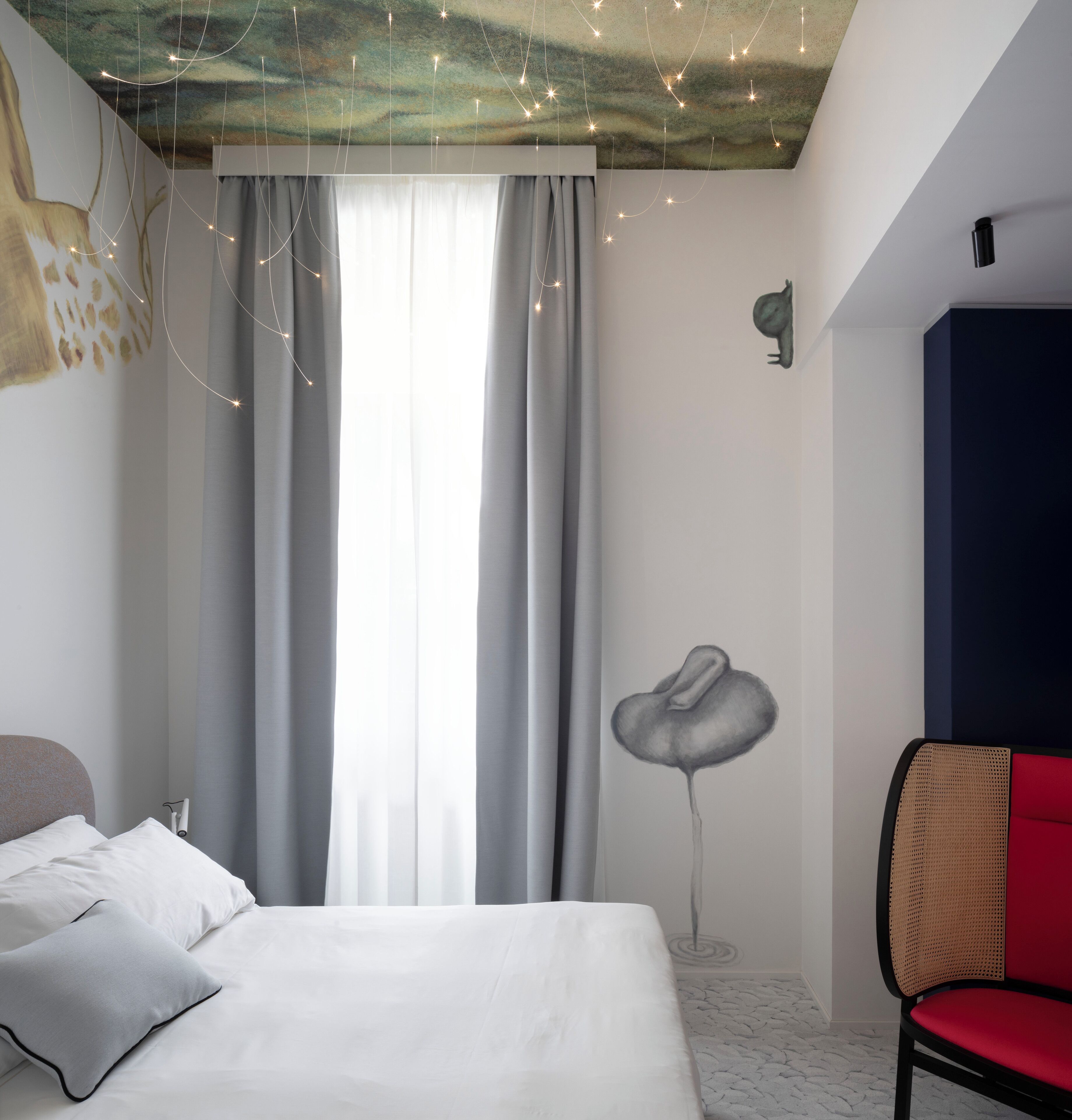 A bedroom with a bed, curtains, a wall-mounted lamp, a chair, and a ceiling mural.