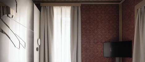 A hotel room with a bed, curtains, a flat-screen TV, and ornate ceiling design.