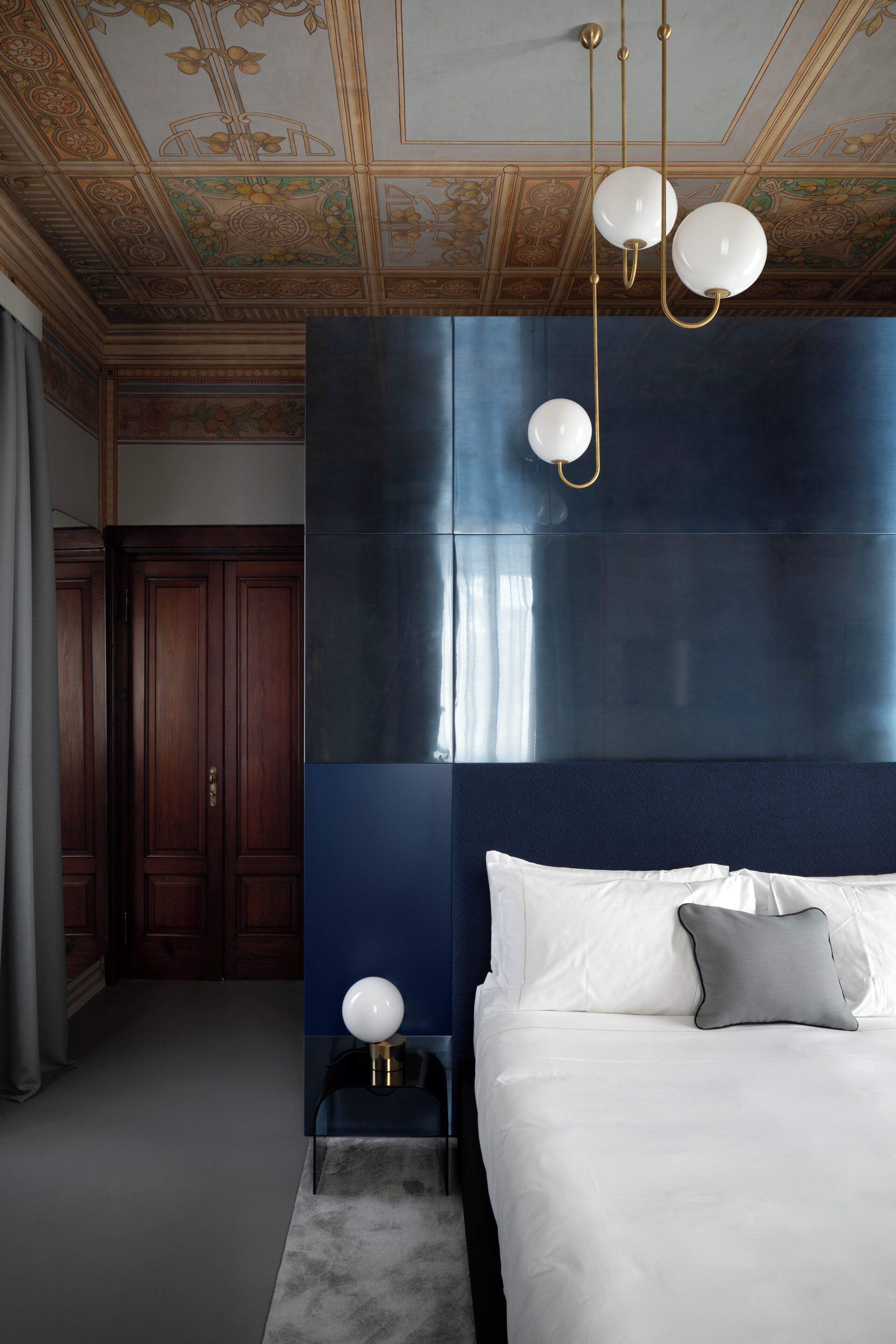 A bedroom with a large bed, a nightstand, a wall-mounted lamp, and a ceiling with intricate designs.