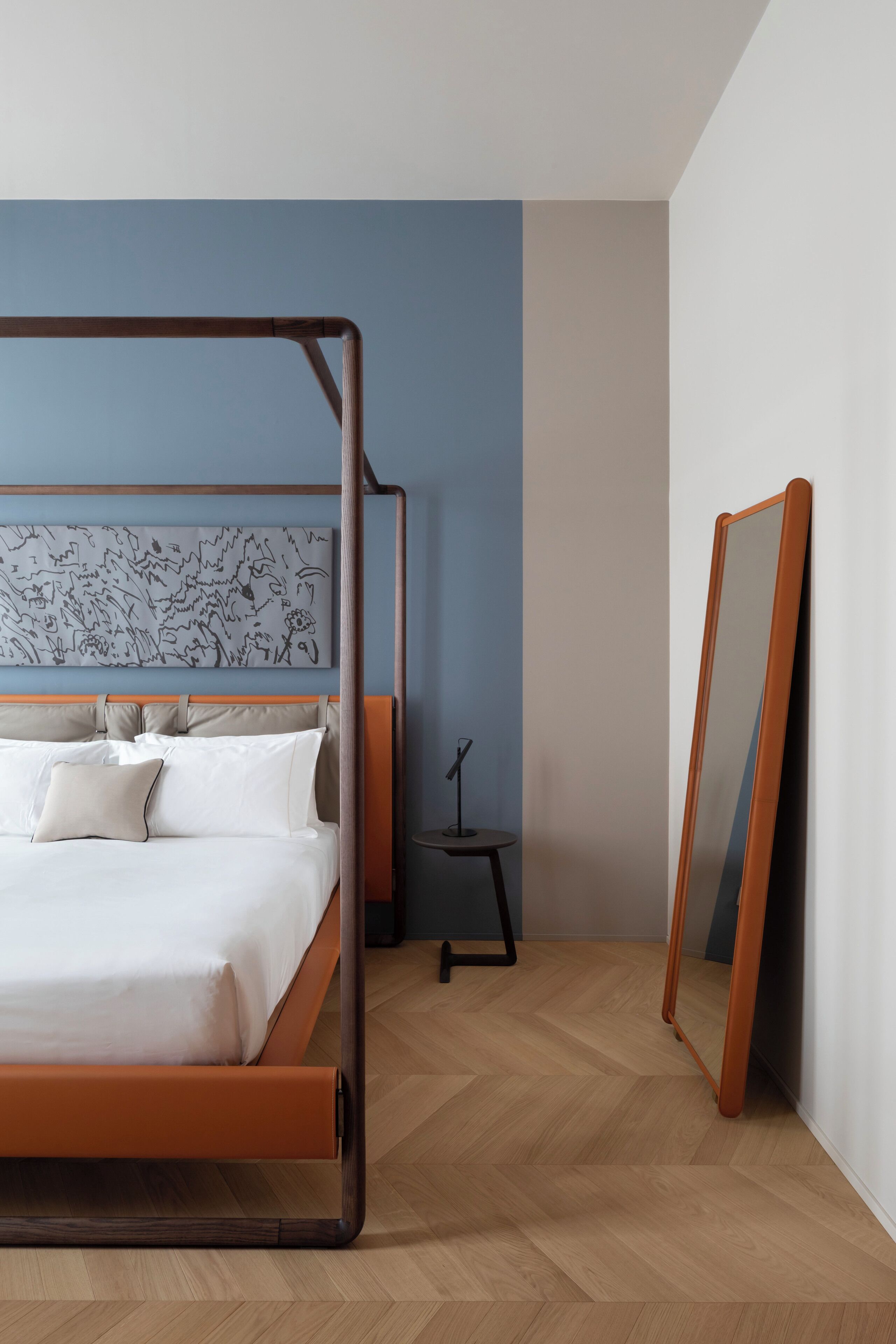 A modern bedroom with a four-poster bed, a large mirror, and a decorative wall piece.