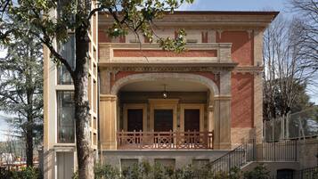 A two-story building with a central entrance, a balcony, and a garden area with gravel and plants.