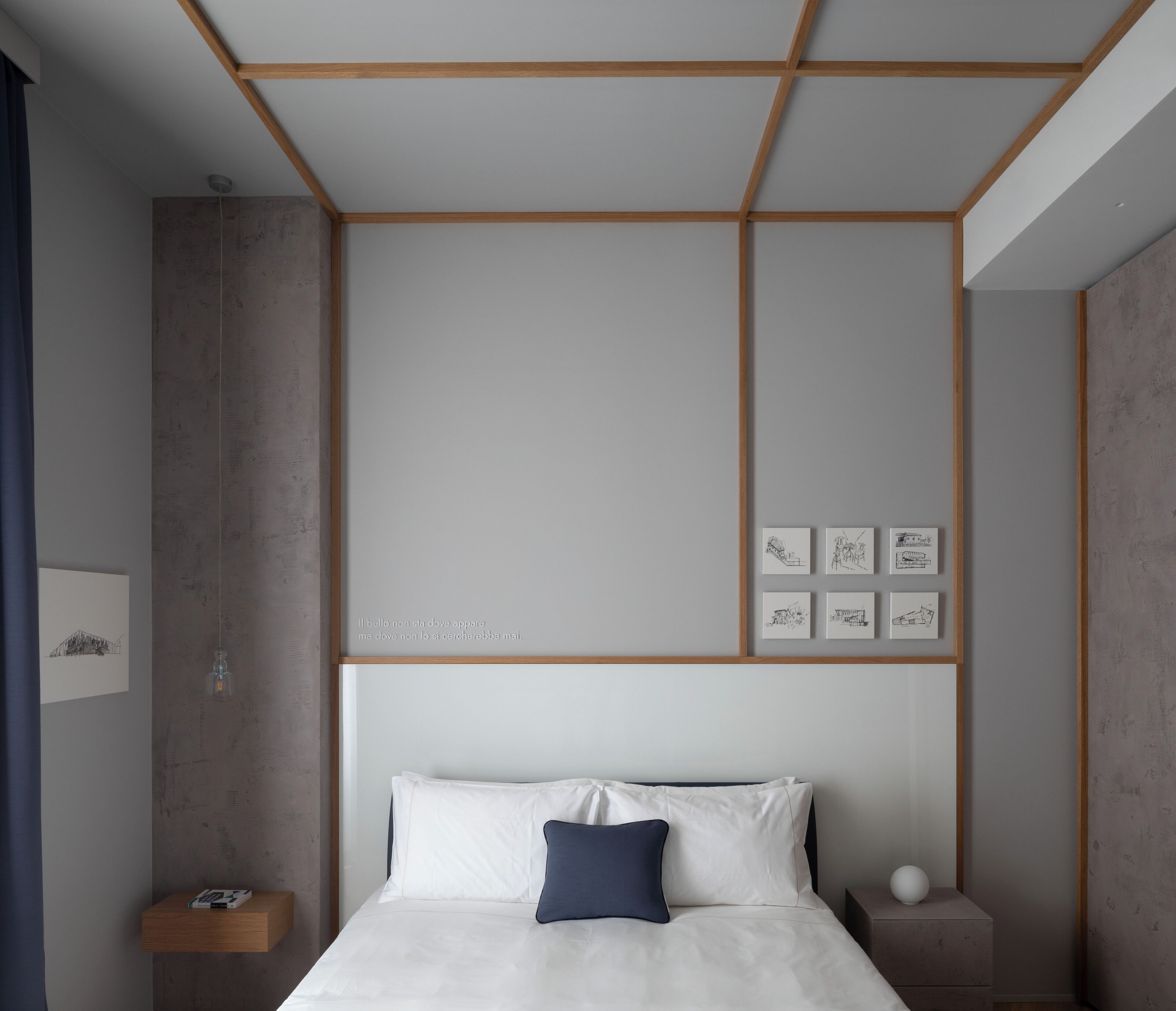Un dormitorio moderno con una cama centrada bajo un diseño geométrico en el techo, una mesita de noche con una lámpara y cuadros en la pared.
