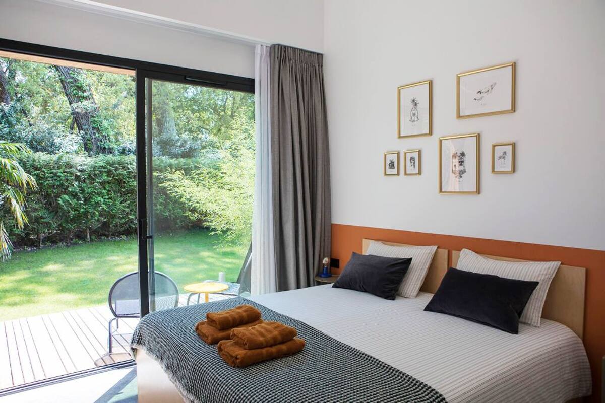 A hotel room with a large bed, a view of a garden through a sliding door, and several framed pictures on the wall.