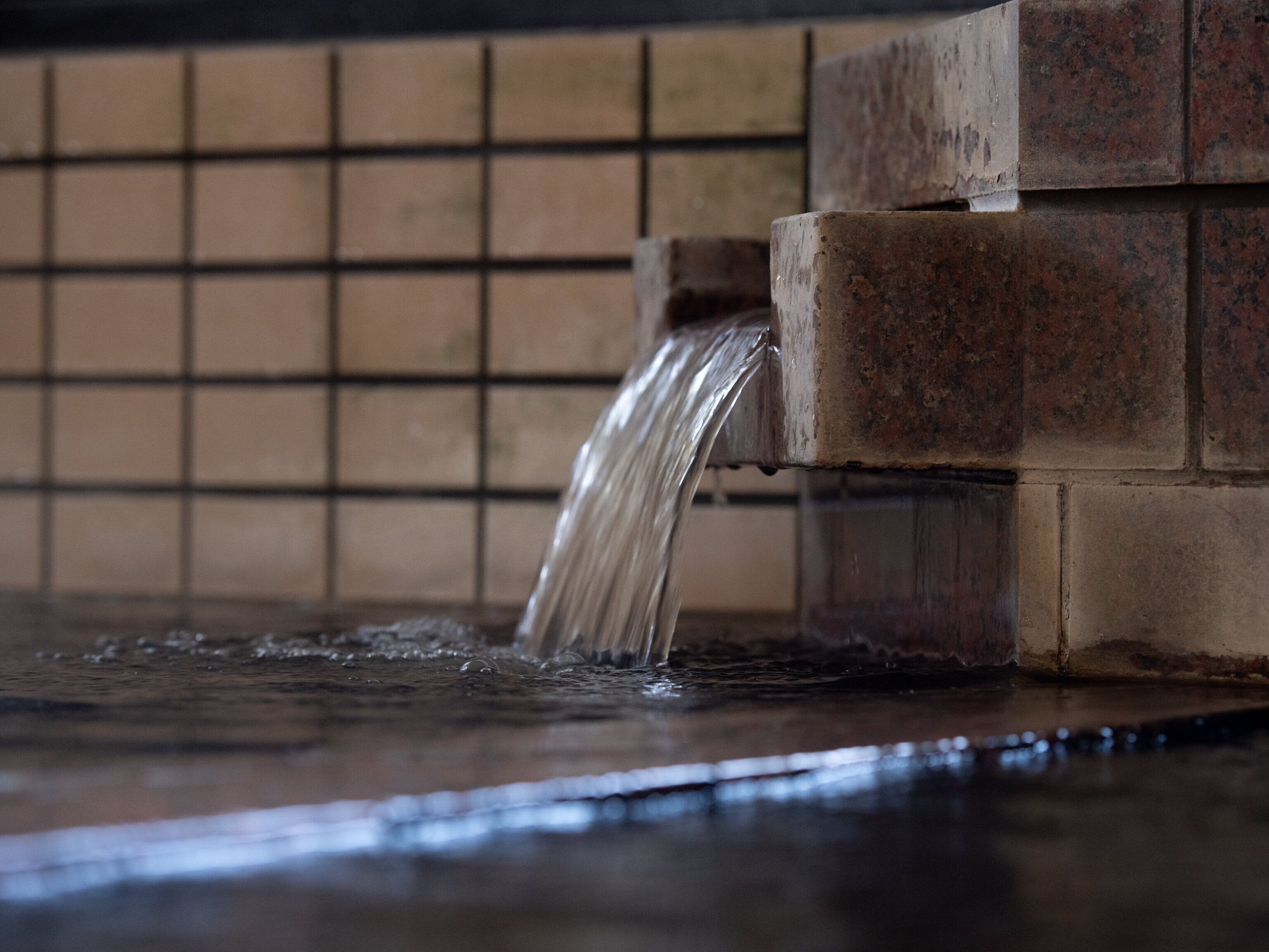 A close-up of a water feature with a tiled wall in the background.