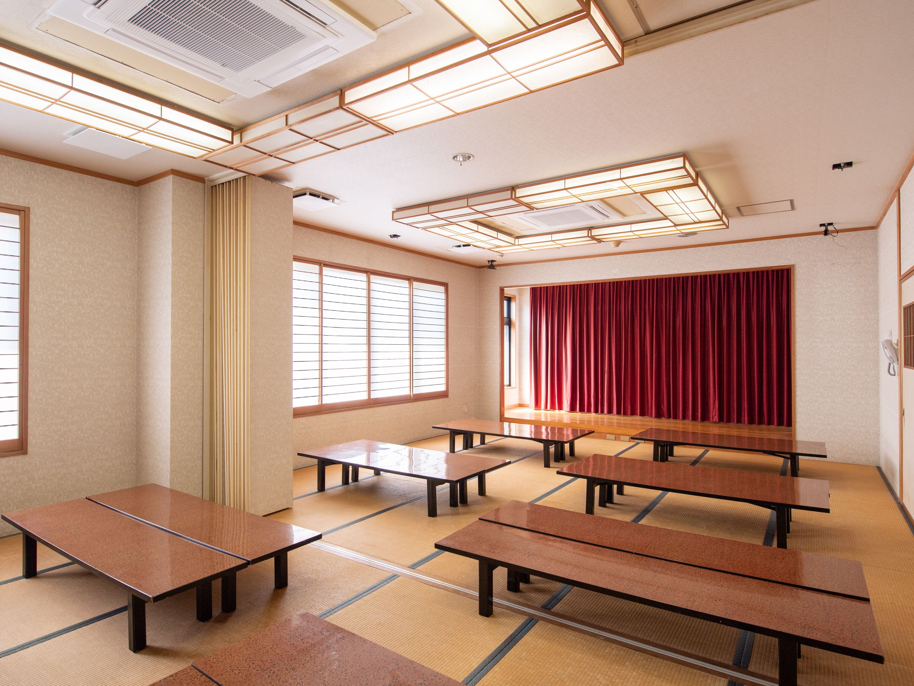 A conference room with multiple tables and a stage with a red curtain.