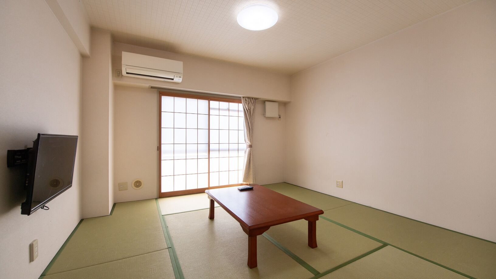 Una habitación con suelo de tatami, puertas correderas, una mesa y un televisor montado.