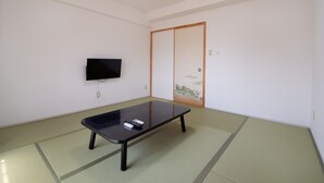 A room with tatami flooring, a low table, a television mounted on the wall, and a sliding door with a traditional design. - Tabist Hotel Yamashiro Onsen (Kofu)