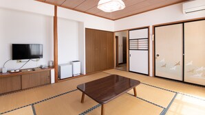 A traditional Japanese room with tatami flooring, a wooden table, a television, and sliding doors. - Tabist Hotel Yamashiro Onsen (Kofu)