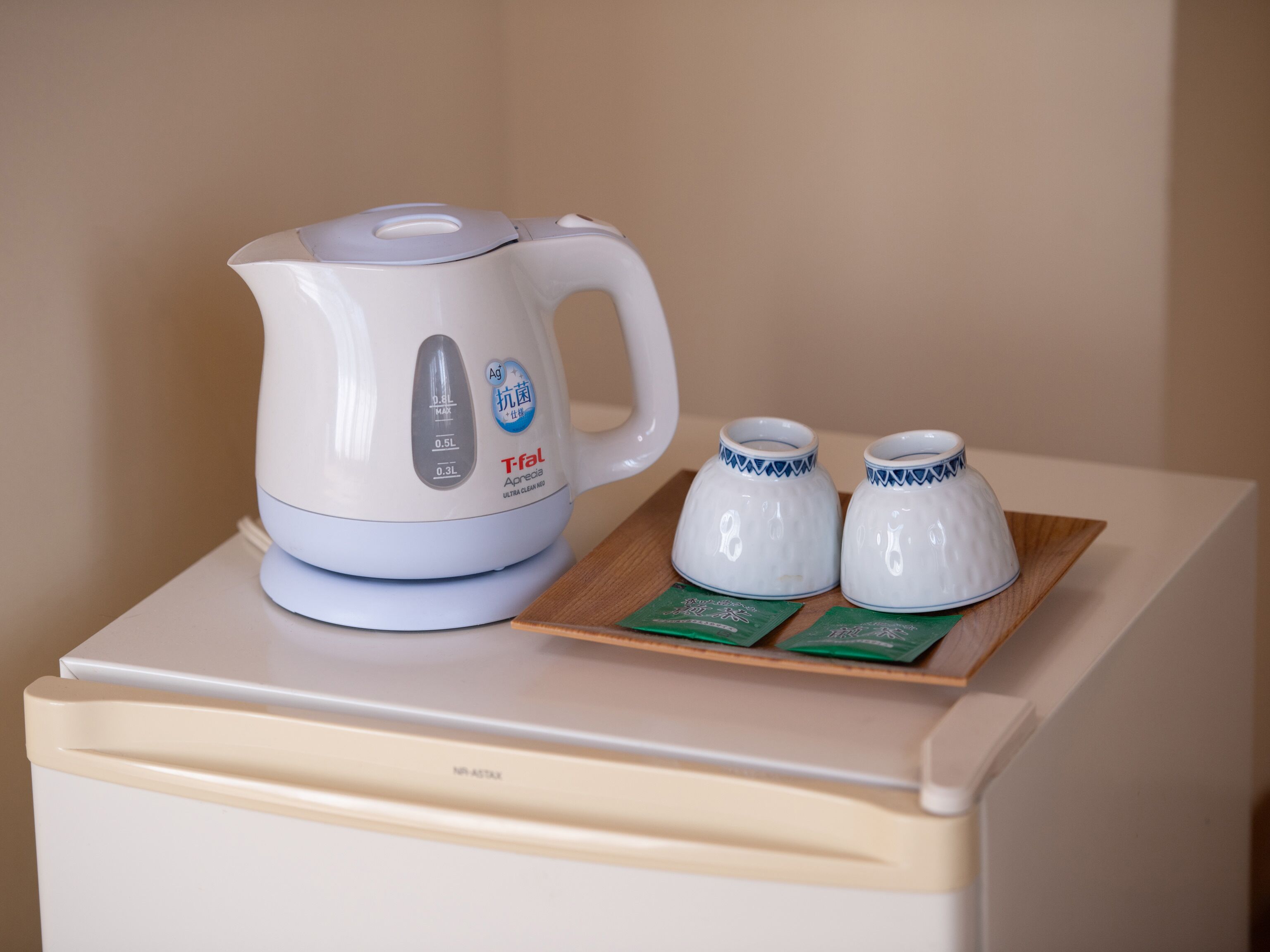 Un brollador elèctric blanc amb una capacitat de 0,8L, 0,5L i 0,3L, col·locat sobre un safata de fusta amb dues tasses petites blanques i dues targetes verdes damunt un taulell beix.