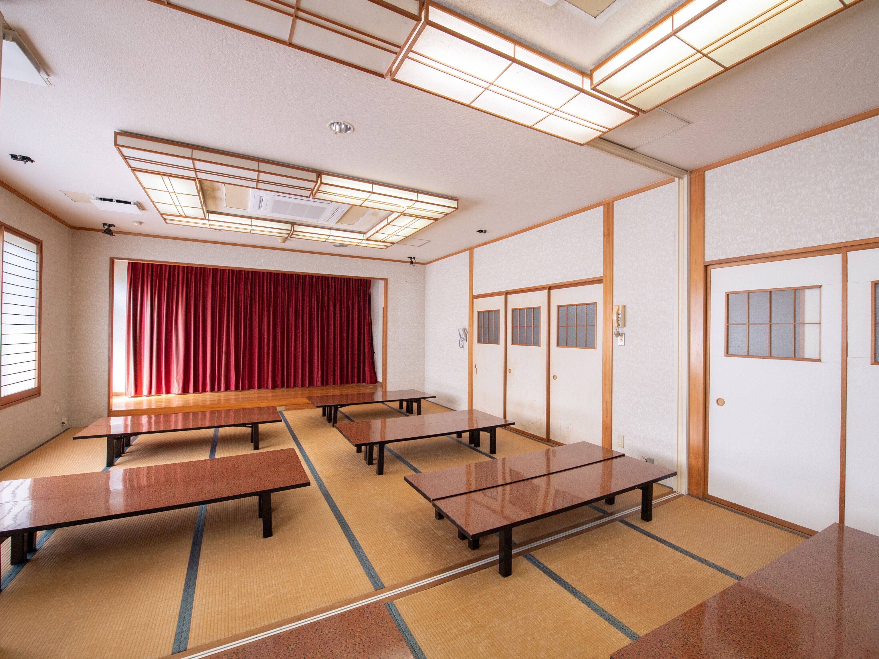 A traditional Japanese room with tatami mats, wooden tables, a red curtain, and sliding doors.