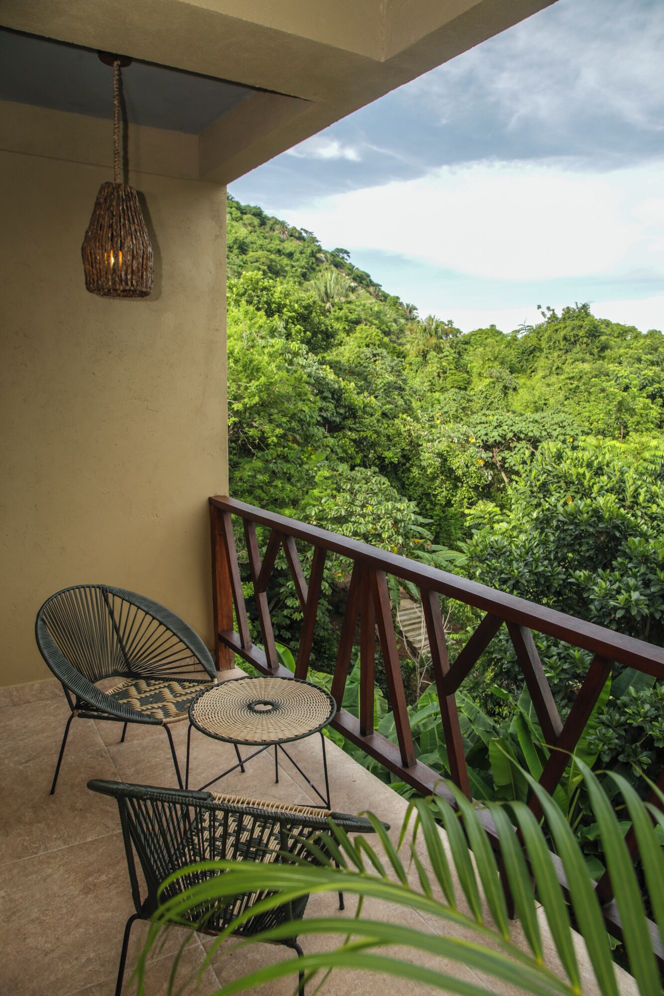 A balcony with wicker furniture, a hanging light fixture, and a view of a lush green landscape.
