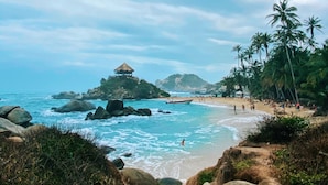 A beach with rocky terrain, palm trees, and a thatched-roof hut. - Villa tayrona (Santa Marta)