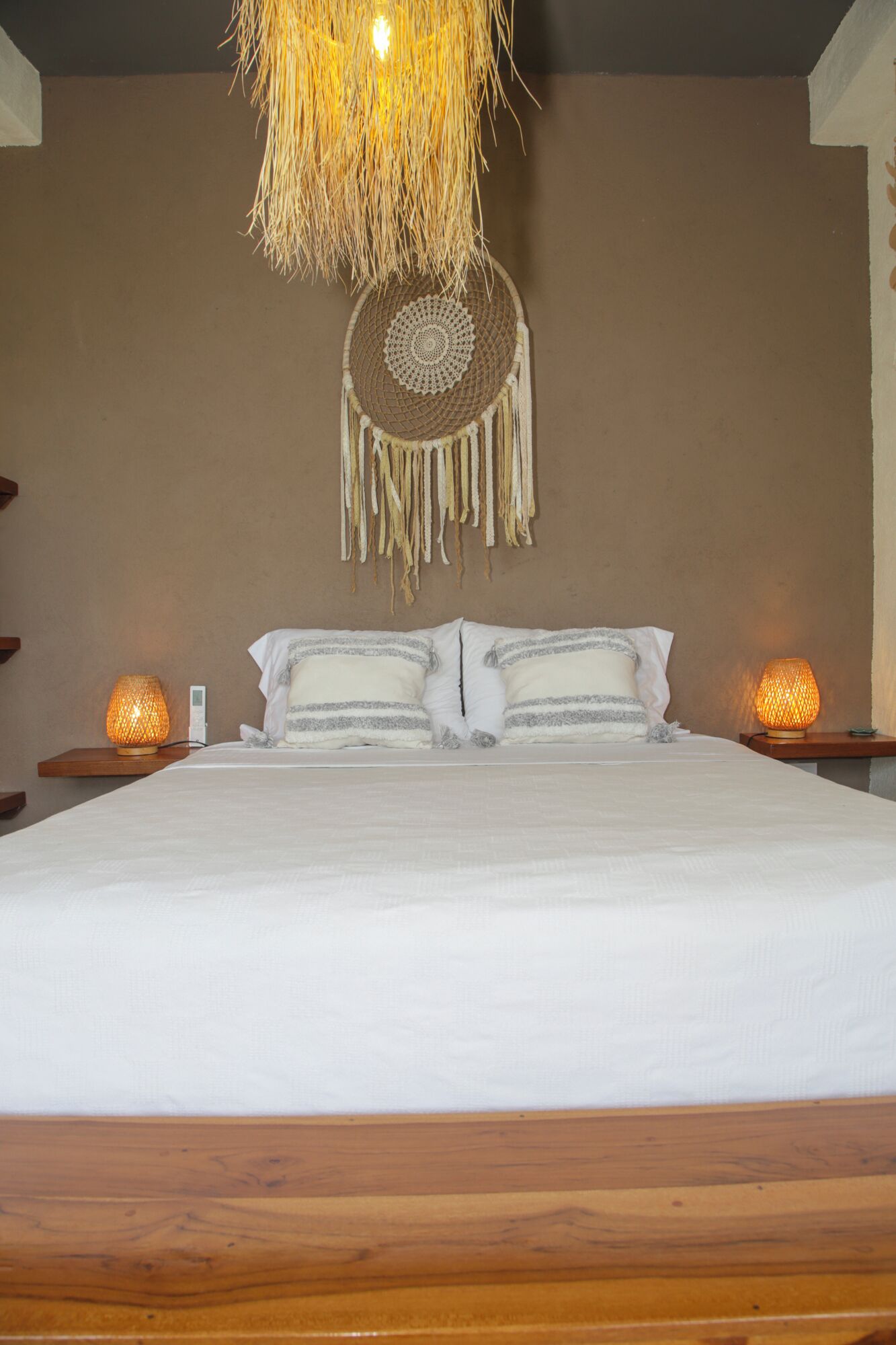 A neatly made bed with white linens, two bedside lamps, and a hanging dreamcatcher.