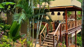 Un espacio al aire libre cubierto con una escalera de madera que lleva a una terraza, rodeado de abundante follaje y diversas plantas.