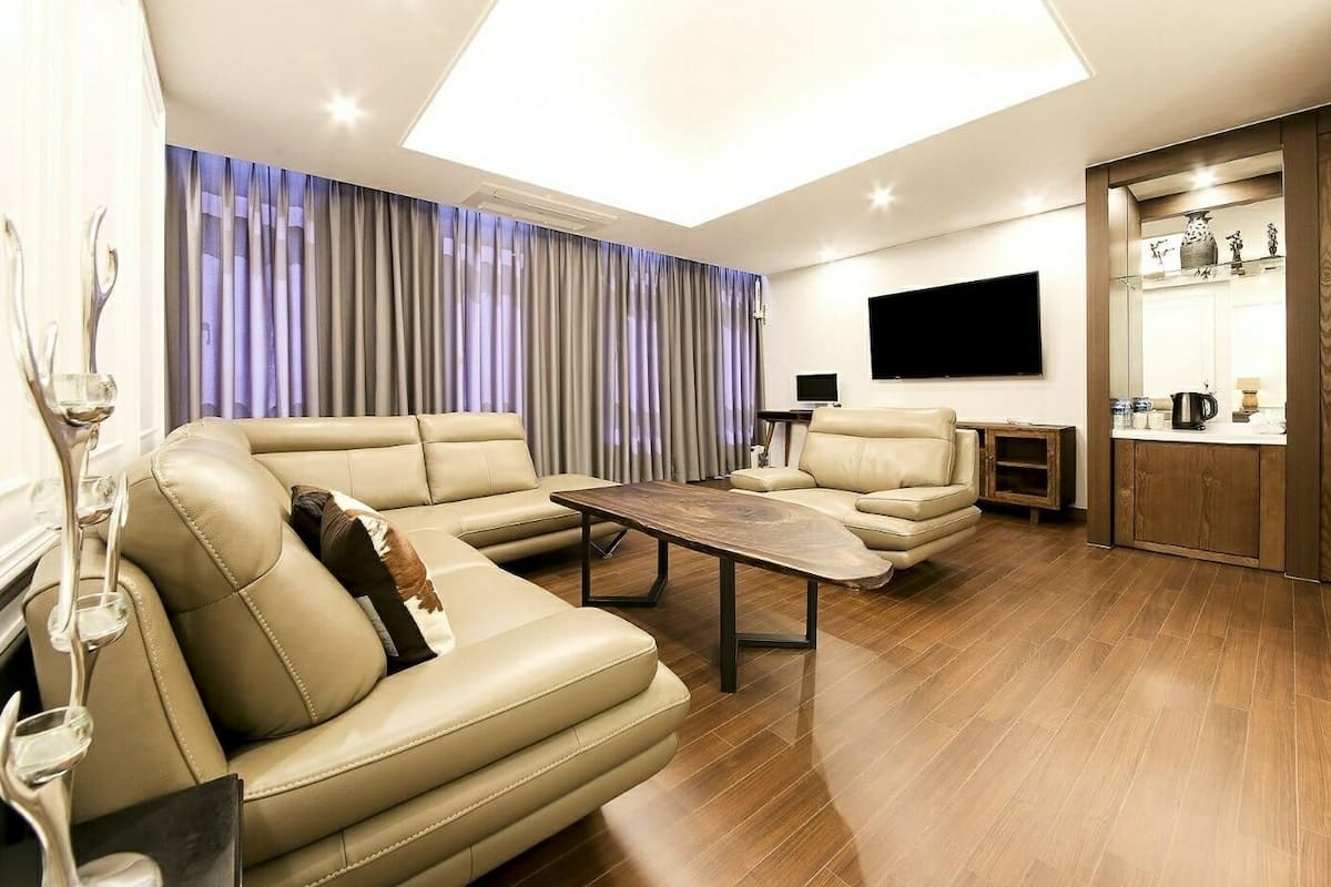 A modern living room with a sectional sofa, a coffee table, and a flat-screen TV mounted on the wall.