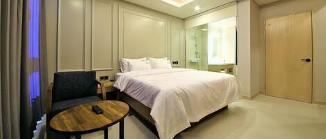 A hotel room with a bed, a small table, a chair, a nightstand, and a wardrobe.