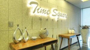 A reception area with a 'Time Square' sign, wooden tables with decorative vases, and a large potted plant. - Time Square Hotel (Yangsan)