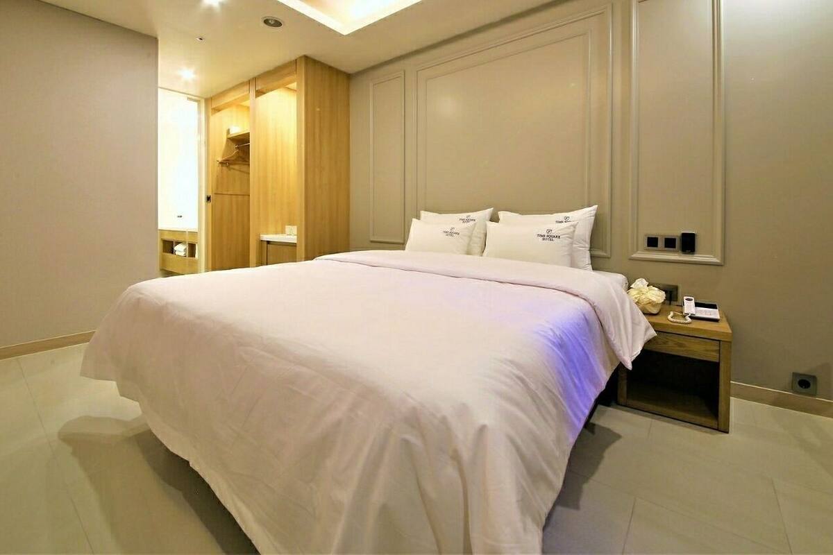 A hotel room with a large bed, a wooden wardrobe, and a bedside table with a lamp.