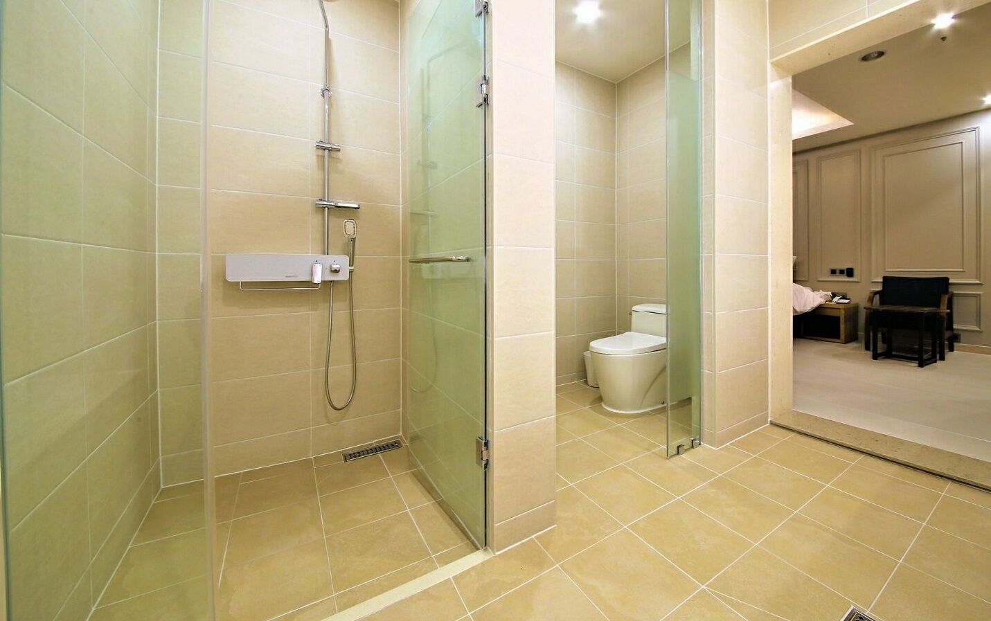 Ein modernes Badezimmer mit einer gläsernen Duschkabine, einer Toilette und einem Frisebereich inklusive Stuhl und kleinem Tisch.
