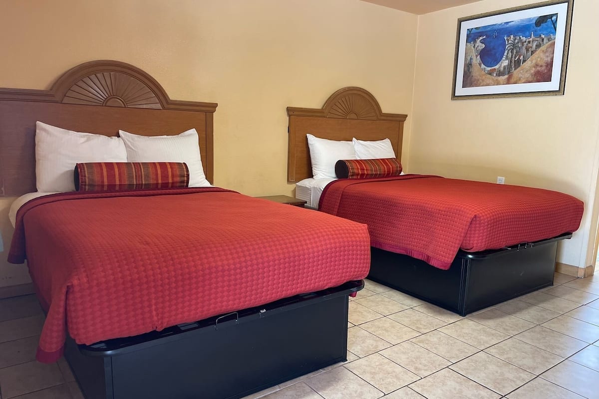 Two single beds with wooden headboards, red bedding, and a painting on the wall.