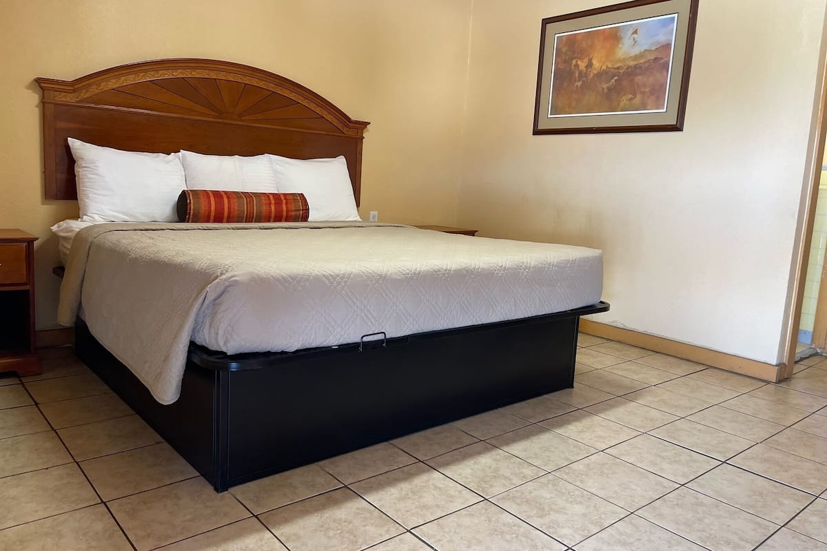 A neatly made bed with a wooden headboard, a small bedside table, and a framed picture on the wall.