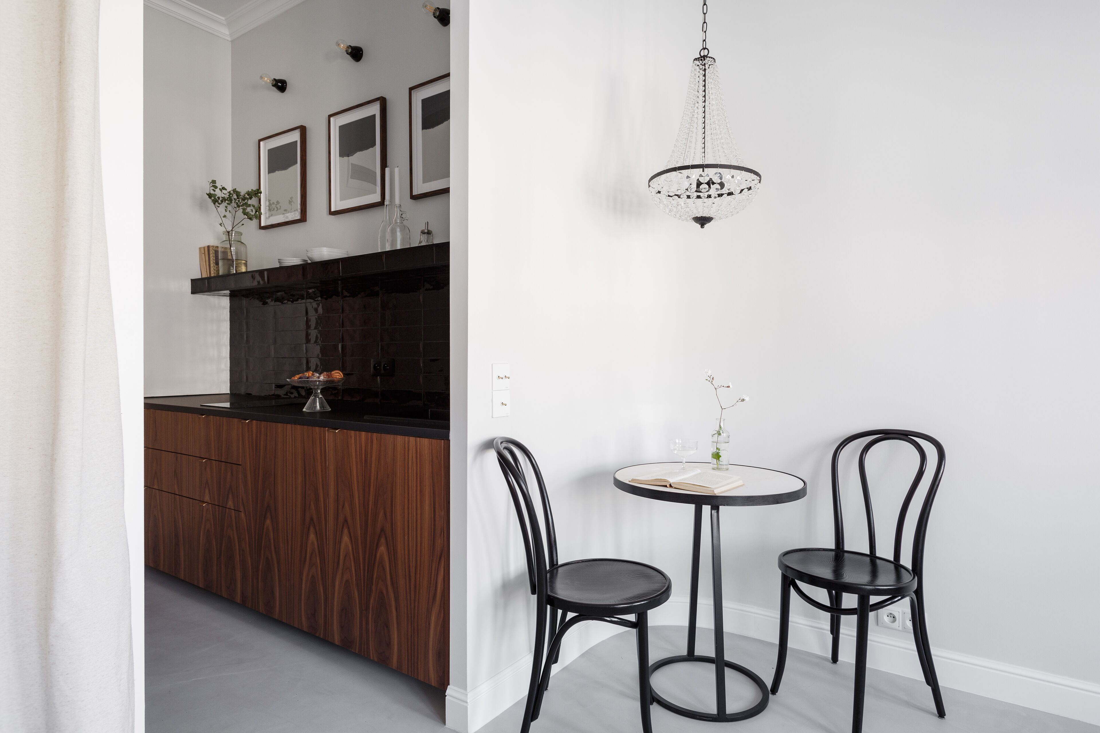 A modern kitchen with a wooden island, a round dining table with two chairs, and a chandelier.